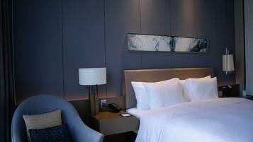 Una habitación de hotel con una cama, una silla, una mesita de noche con lámpara y una obra de arte en la pared.