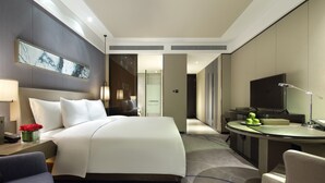 Una habitación de hotel moderna con una cama grande, un escritorio con lámpara, un televisor y un baño con espejo y lavamanos.