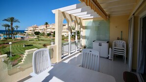Un balcón con vista al mar, muebles blancos y una puerta de cristal.