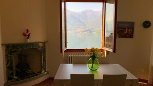 Un coin repas comprenant une table, des chaises, un vase de fleurs, une cheminée et une fenêtre donnant sur des montagnes et un lac.