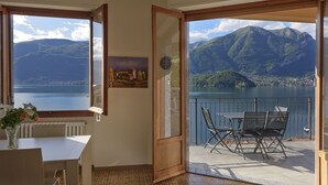 Une pièce avec vue sur un lac et des montagnes, un coin repas avec des chaises et une table, et un tableau accroché au mur.