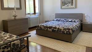 Une chambre à coucher comprenant un lit, une commode, une table de chevet, une lampe, un radiateur, une fenêtre avec des rideaux, un miroir et un tableau accroché au mur.