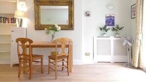 Un coin repas avec une table et des chaises en bois, un miroir doté d’un cadre décoratif, une bibliothèque et un radiateur.