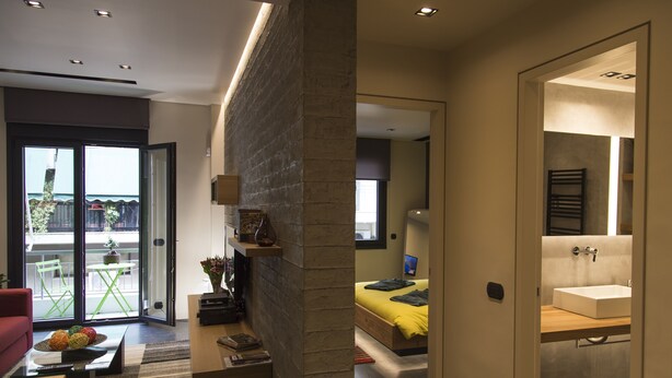 Um interior moderno com uma porta de vidro que dá para uma varanda, uma escrivaninha de madeira e uma cama com colcha amarela.