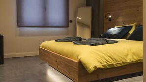 Quarto moderno com estrutura de cama de madeira, uma janela grande com persianas e um aplique na parede.