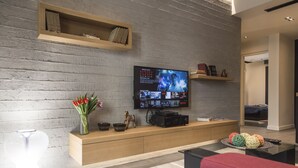 Uma sala de estar moderna com uma TV de tela plana presa em uma parede de tijolos, prateleiras de madeira, um sofá vermelho e uma mesa de centro com bolas decorativas.