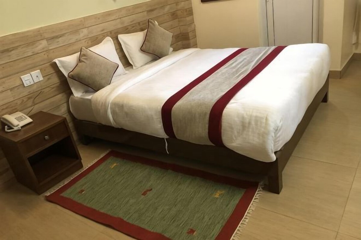 A bed with pillows and a blanket, a nightstand with a phone, and a rug.