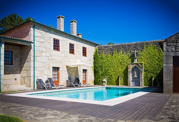 Un bâtiment en pierre doté d’une piscine, de chaises longues et d’une petite chapelle.