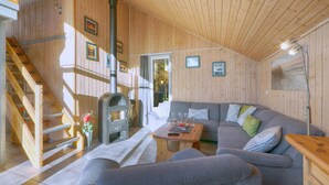 L’intérieur chaleureux d’un chalet avec un escalier en bois, une cheminée, un canapé et une table à manger.
