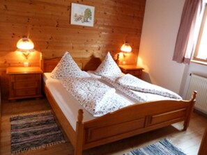 A wooden bed with a white bedspread and pillows, two bedside tables with lamps, and a wooden headboard. - Apartments Leitner, Florian - Apartment Bodenschneid (Schliersee)