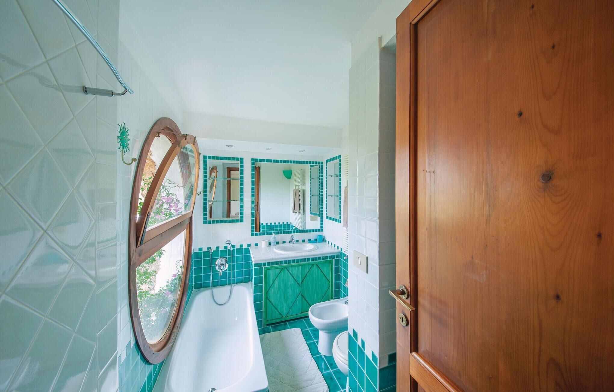 A bathroom with a bathtub, a sink, and a toilet. There is a wooden door and a window with a view of greenery.