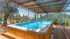Un bain à remous doté d’une structure extérieure en bois et d’une paroi en verre, entouré d’une terrasse en bois et offrant une vue sur un paysage montagneux.