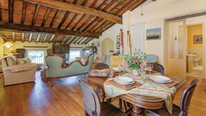 Un coin repas accueillant, avec une table en bois dressée pour deux personnes, entouré de sièges confortables. Un téléviseur est fixé au mur, et une fenêtre laisse entrer la lumière naturelle.