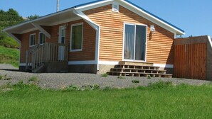A single-story wooden house with a sloped roof, a front porch with a railing, and a wooden fence.