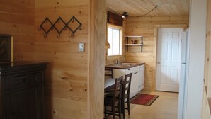 A wooden cabin interior with a kitchen area, including a dining table and chairs, a sink, and a refrigerator.