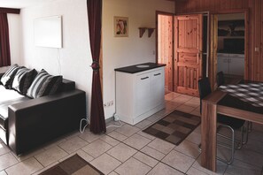 A compact living space with a sofa, a kitchenette, a dining area, and a wooden door leading to another room.