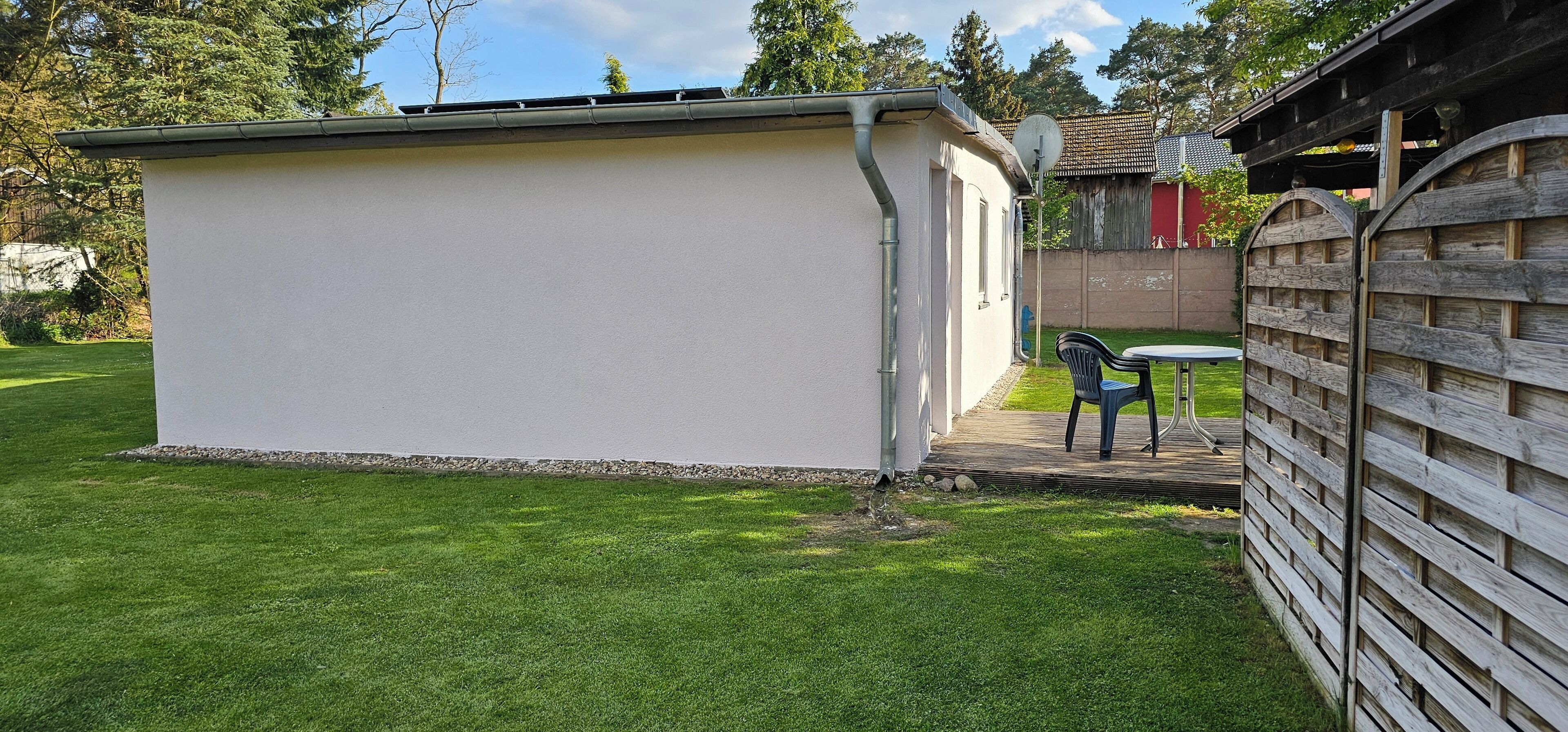 Een klein, wit, laag gebouw met een plat dak, een schotelantenne en een klein terras met een tafel en stoel.