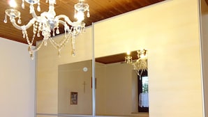 Une chambre avec un plafond en bois, un lustre, un lit avec une literie bleue et à motifs floraux, et un grand miroir.