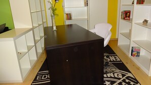 Une pièce avec un bureau noir, des étagères blanches et un tapis à motifs.