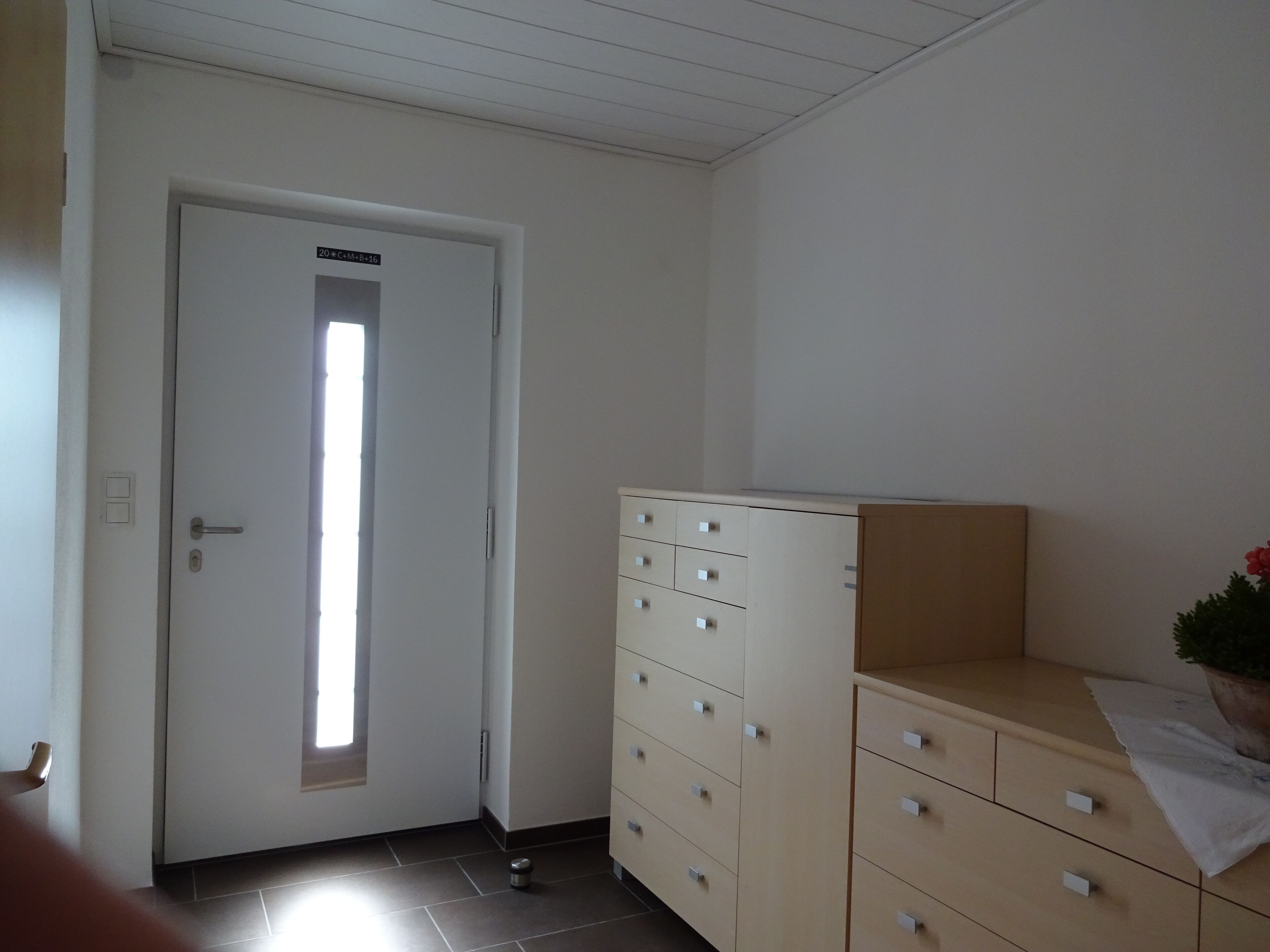 A room with a white door, a small window, a beige cabinet with drawers, and a tiled floor.