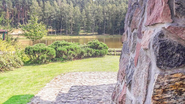 Un muro de piedra con un camino de piedra que lleva a un lago rodeado de árboles.