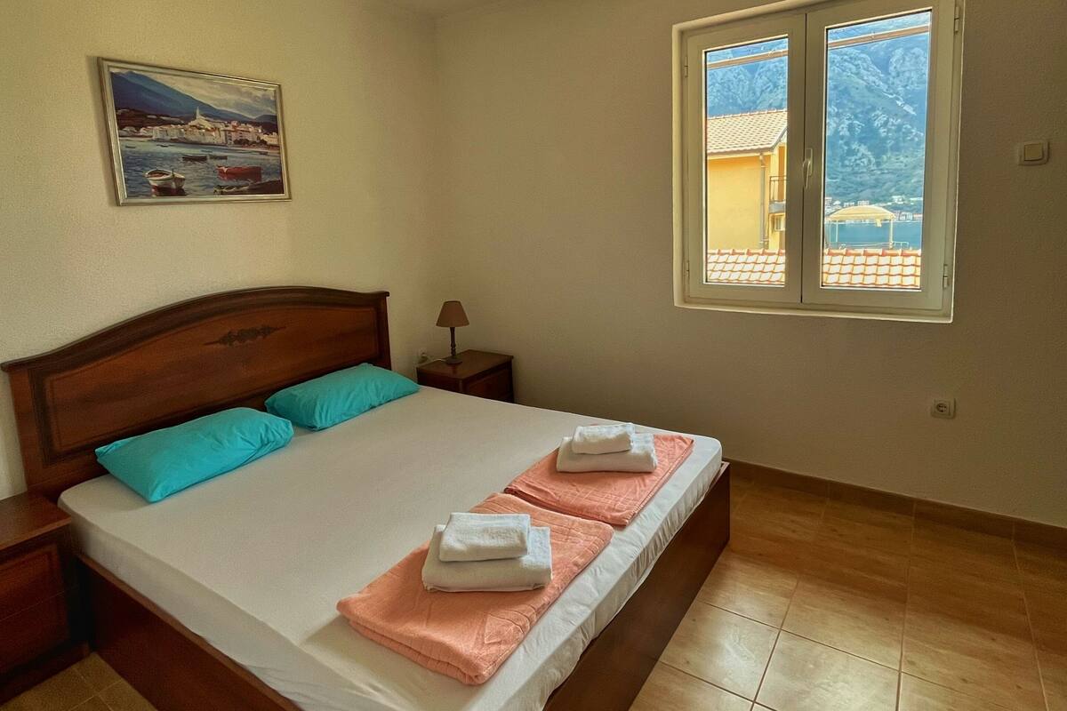 Quarto com cama de madeira, um quadro, janela com vista e luminária no teto.