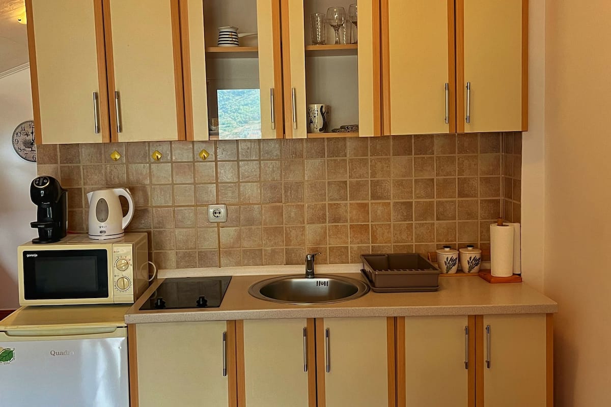 Cozinha compacta com armários de madeira, micro-ondas, chaleira e pia.