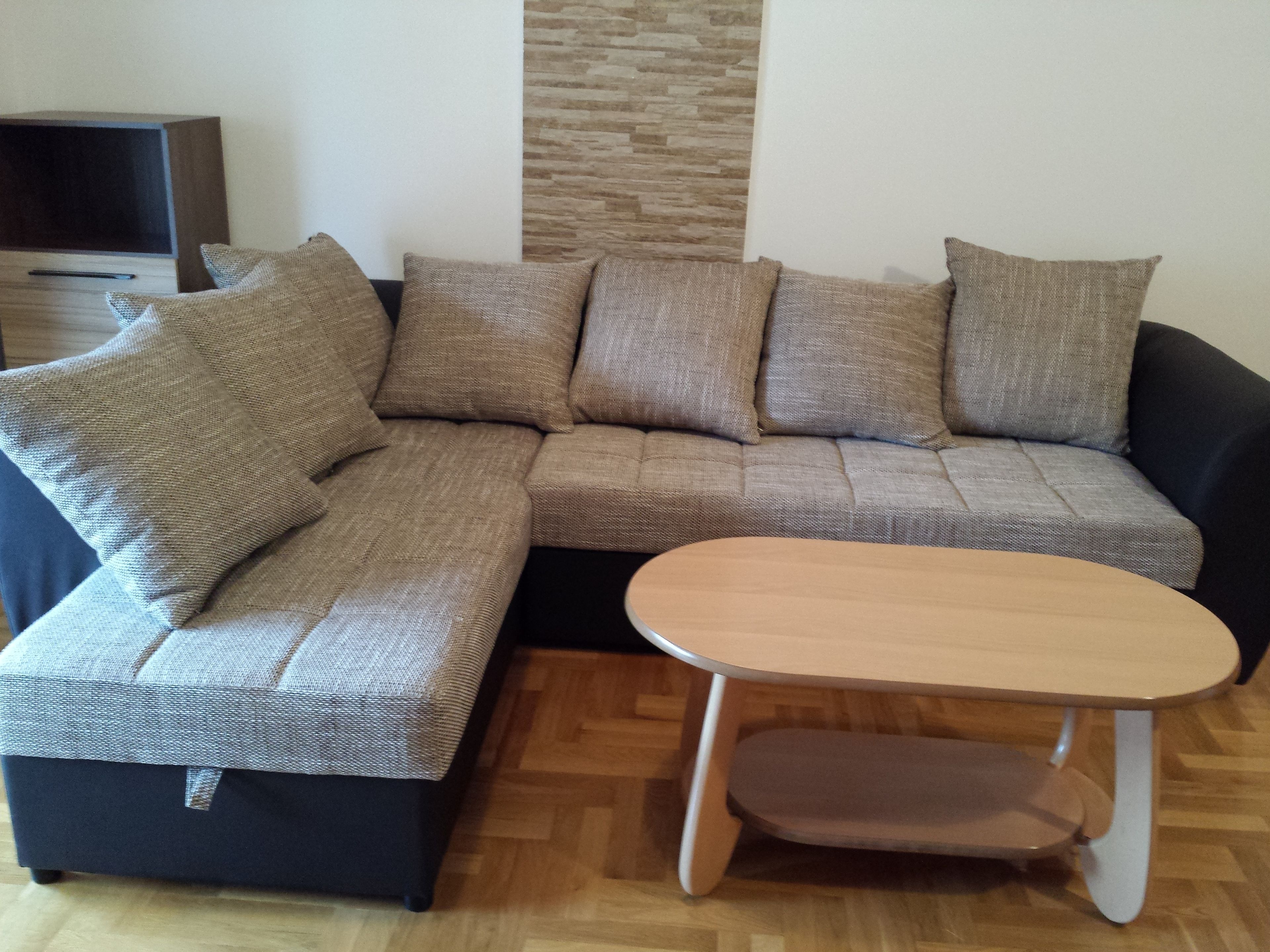Un canapé modulable avec plusieurs coussins, une petite table en bois et un téléviseur à l’arrière-plan.