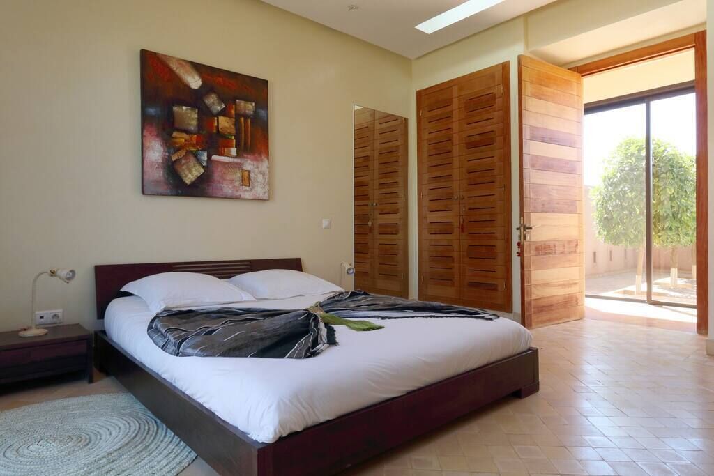 Un dormitorio con cama, mesita de noche, un cuadro y puerta corredera que da a un espacio exterior.