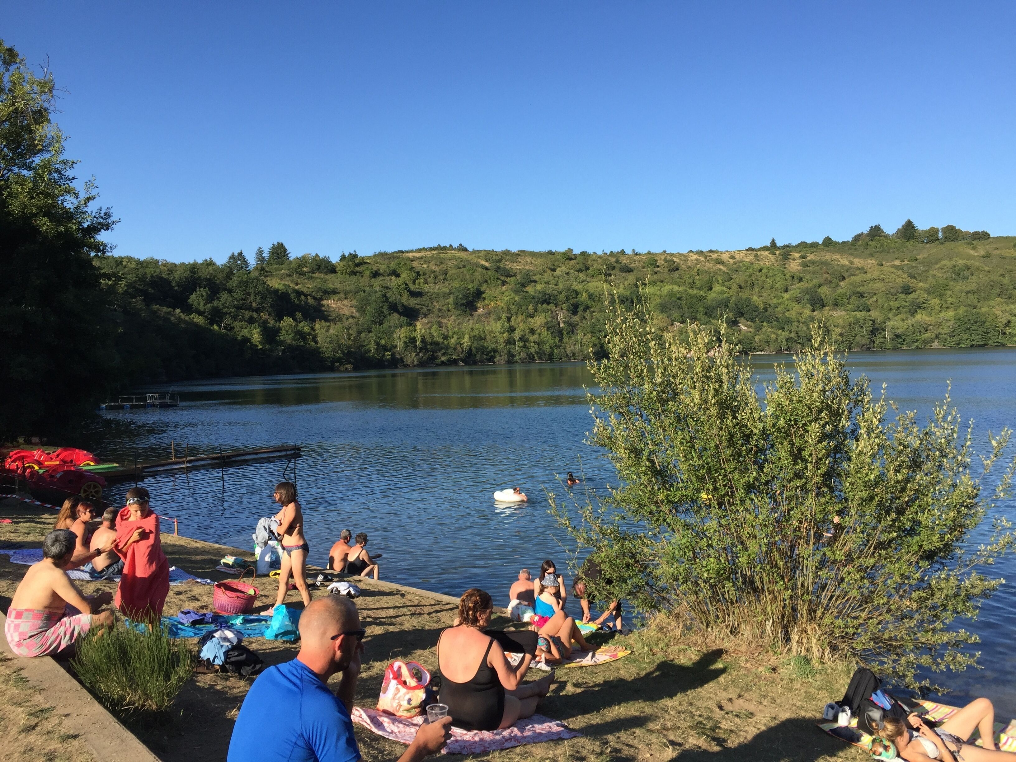 Une scène au bord d’un lac, où l’on voit des gens se détendre près de l’eau, certains sur la rive et d’autres dans l’eau.