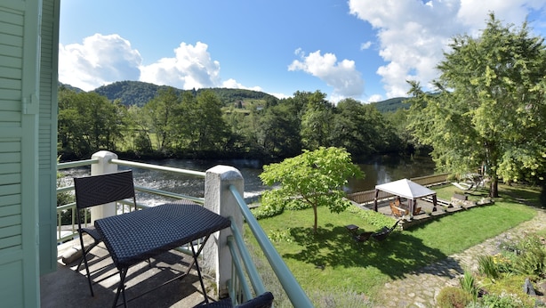 Ein Balkon mit Blick auf einen Fluss, ein Gazebo und eine begrünte Fläche mit Bäumen.