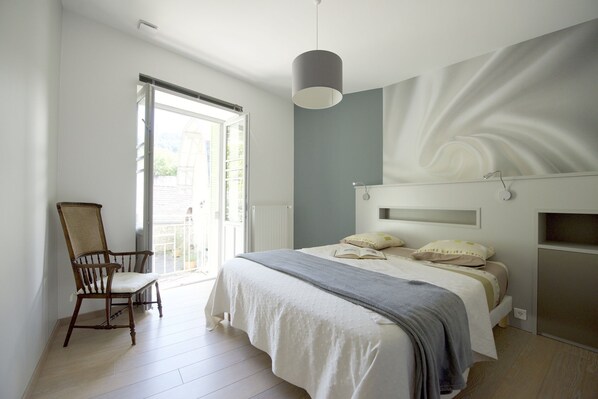 A bedroom with a bed, a chair, a window, and a wall with a light fixture.