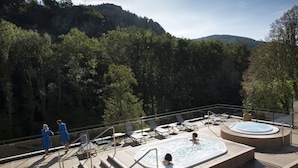 Eine Terrasse mit Whirlpools und Liegestühlen mit Blick auf eine bewaldete Landschaft.