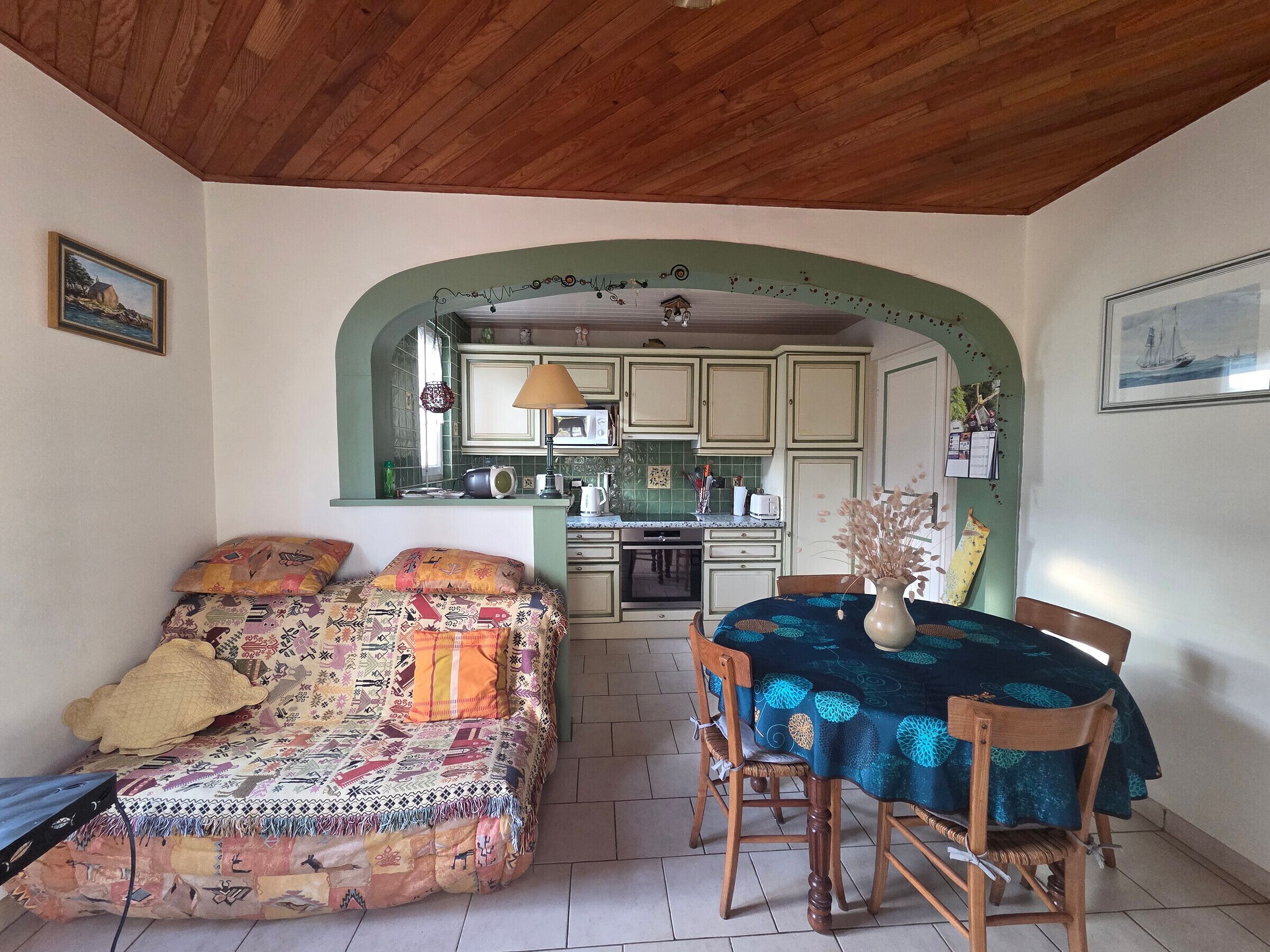 Una habitación acogedora con cama, una mesa de comedor con sillas, una zona de cocina y techo de madera.