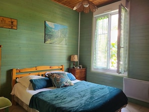 Um quarto com uma cama de madeira, uma mesa de cabeceira, um abajur, uma janela com cortinas e uma parede verde.