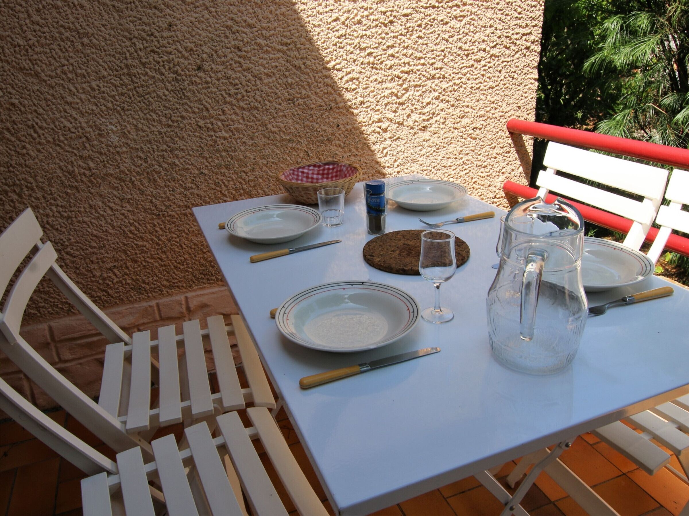 A table set outdoors with plates, cutlery, a glass, a pitcher, and a basket.
