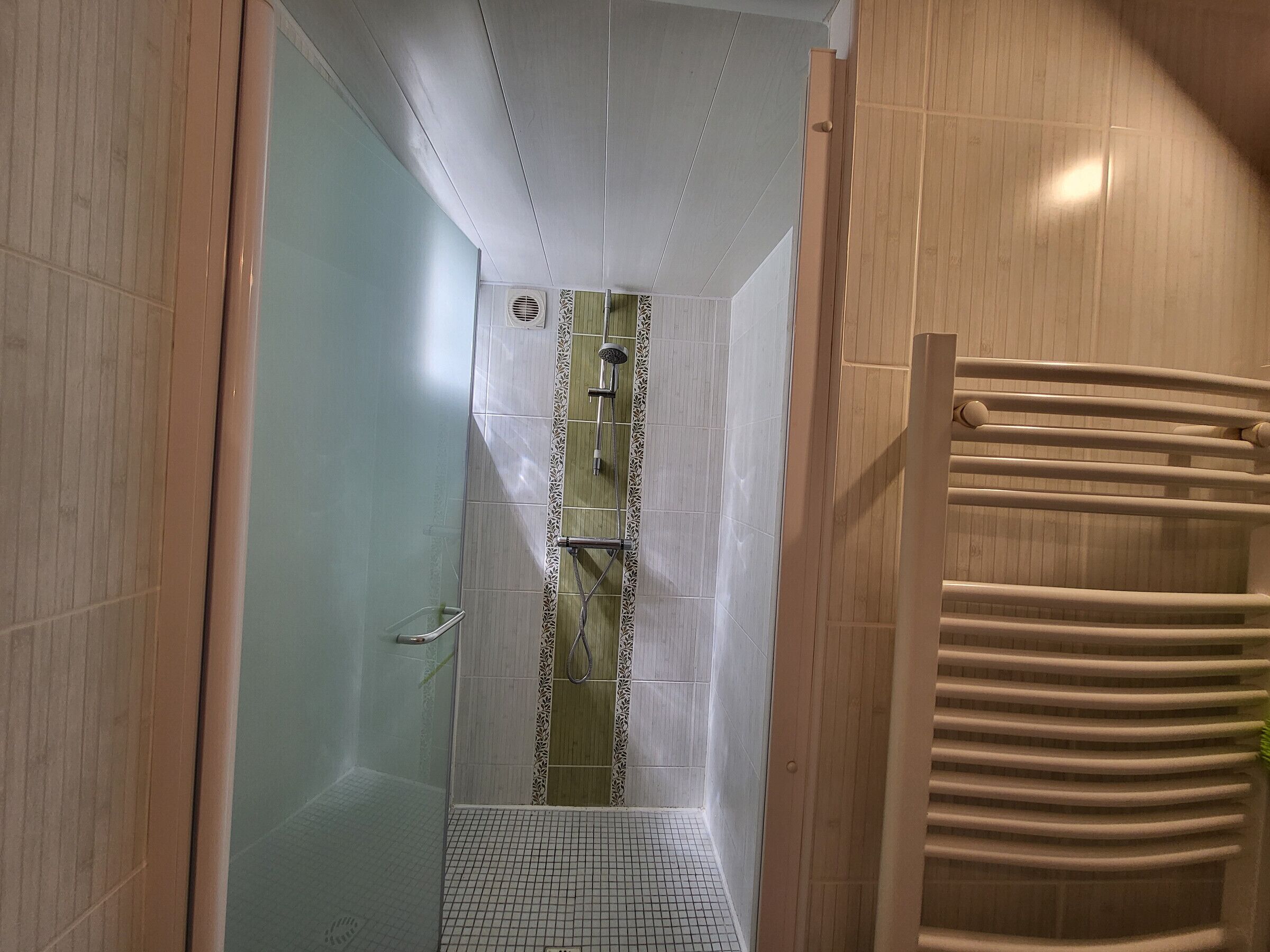Une salle de bain moderne avec une douche à parois de verre, un porte-serviettes en bois et un carrelage au sol.