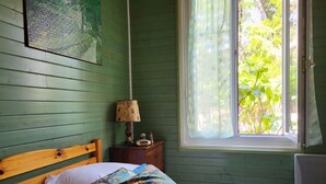 Ein Schlafzimmer mit einem hölzernen Bett, einem Nachttisch mit Lampe und einem Fenster mit Blick ins Grüne.