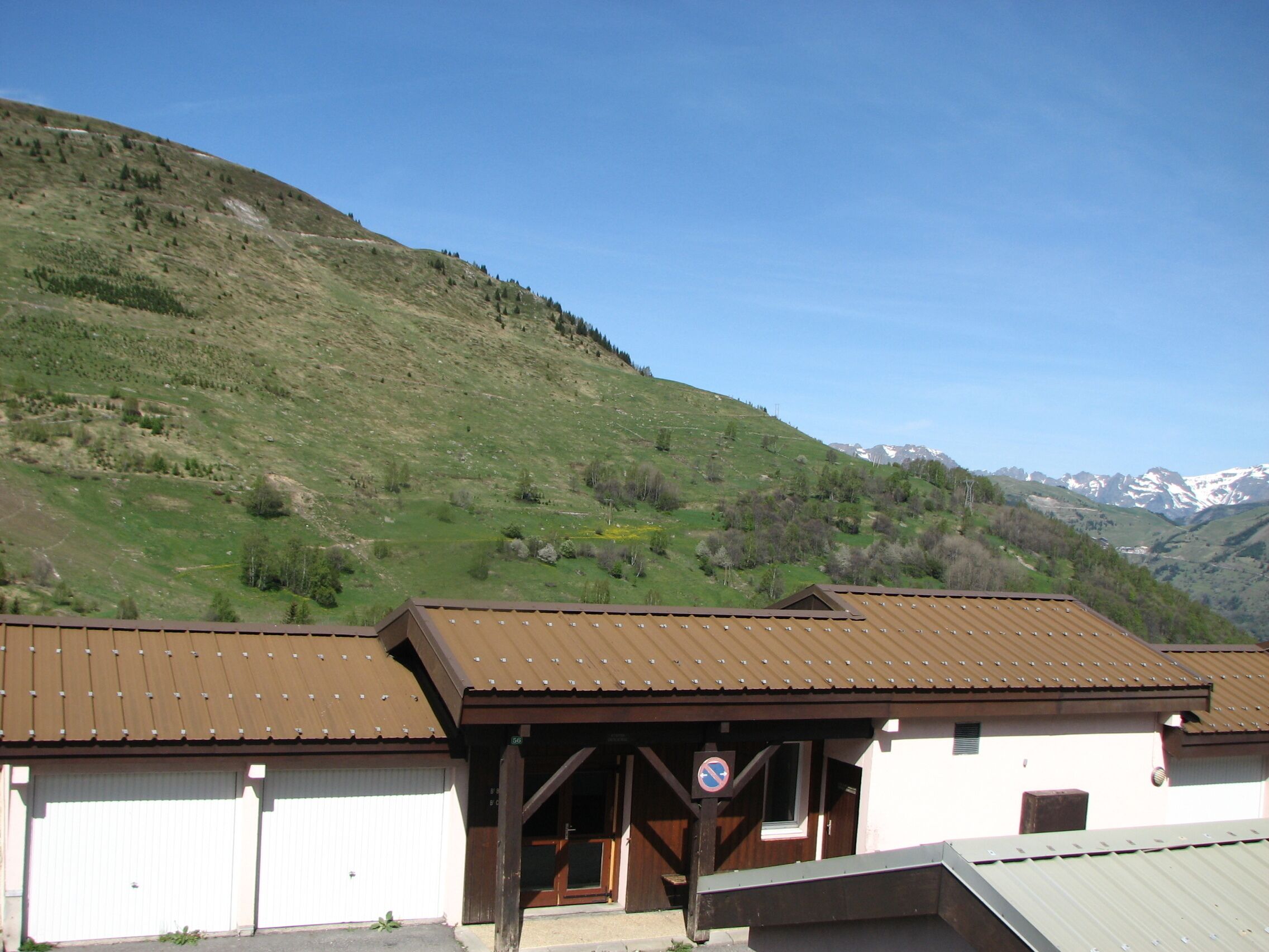 Un edificio con techo marrón y paredes blancas, un cartel de 'no estacionar' y un paisaje montañoso de fondo.