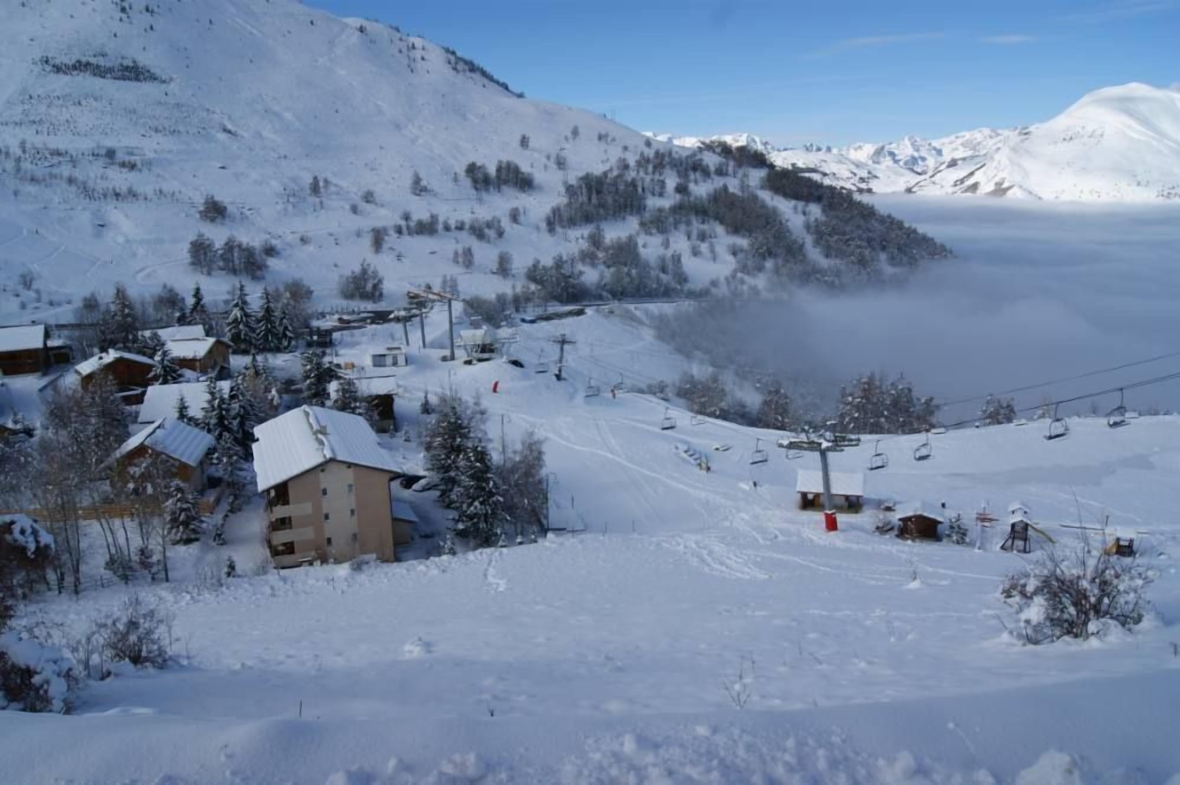 Un village de montagne enneigé, avec des maisons, un télésiège et un ciel dégagé.