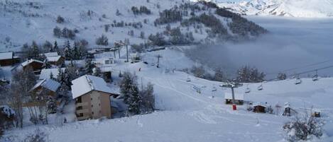 A snow-covered mountain village with houses, a ski lift, and a clear sky.
