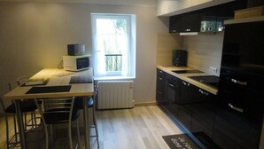 A compact kitchen with a dining area, a window with a view, and a black refrigerator. - Gîte au Moulin (Loft) Pets welcome!  (Naucelle)