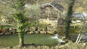 A rustic stone bridge over a small stream, surrounded by trees and a wooden structure in the background. - Gîte au Moulin (Loft) Pets welcome!  (Naucelle)