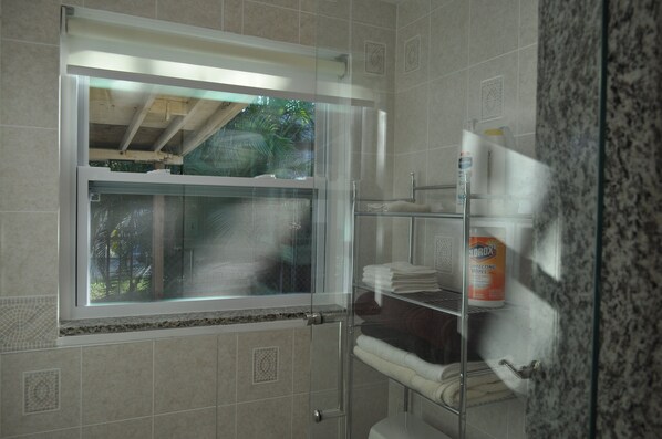 A bathroom with a window, a shelf with towels, and a bottle of disinfecting wipes.