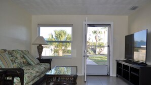 Un salon comprenant un canapé, une table basse, un téléviseur et une porte donnant sur un balcon avec vue sur des palmiers.