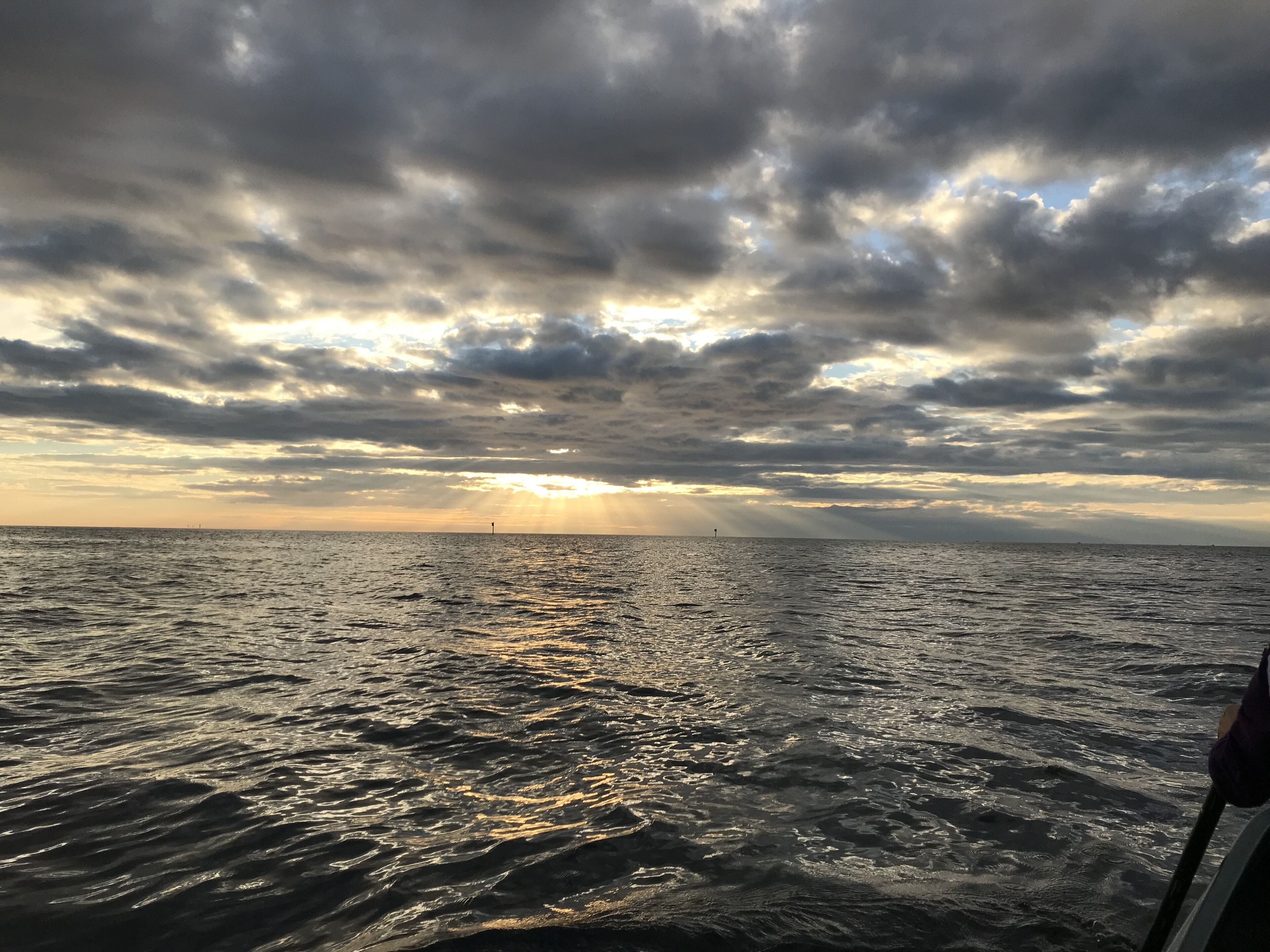 A view of the ocean with a boat in the foreground and a lighthouse in the distance under a cloudy sky.