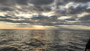 A view of the ocean with a boat in the foreground and a lighthouse in the distance under a cloudy sky.