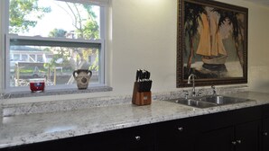 Une cuisine dotée d’un plan de travail en granit, d’un évier, d’une fenêtre donnant sur l’extérieur et d’un tableau accroché au mur.