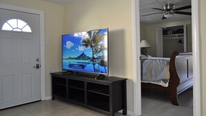 Une chambre à coucher avec un lit, un téléviseur posé sur un meuble et un ventilateur de plafond.
