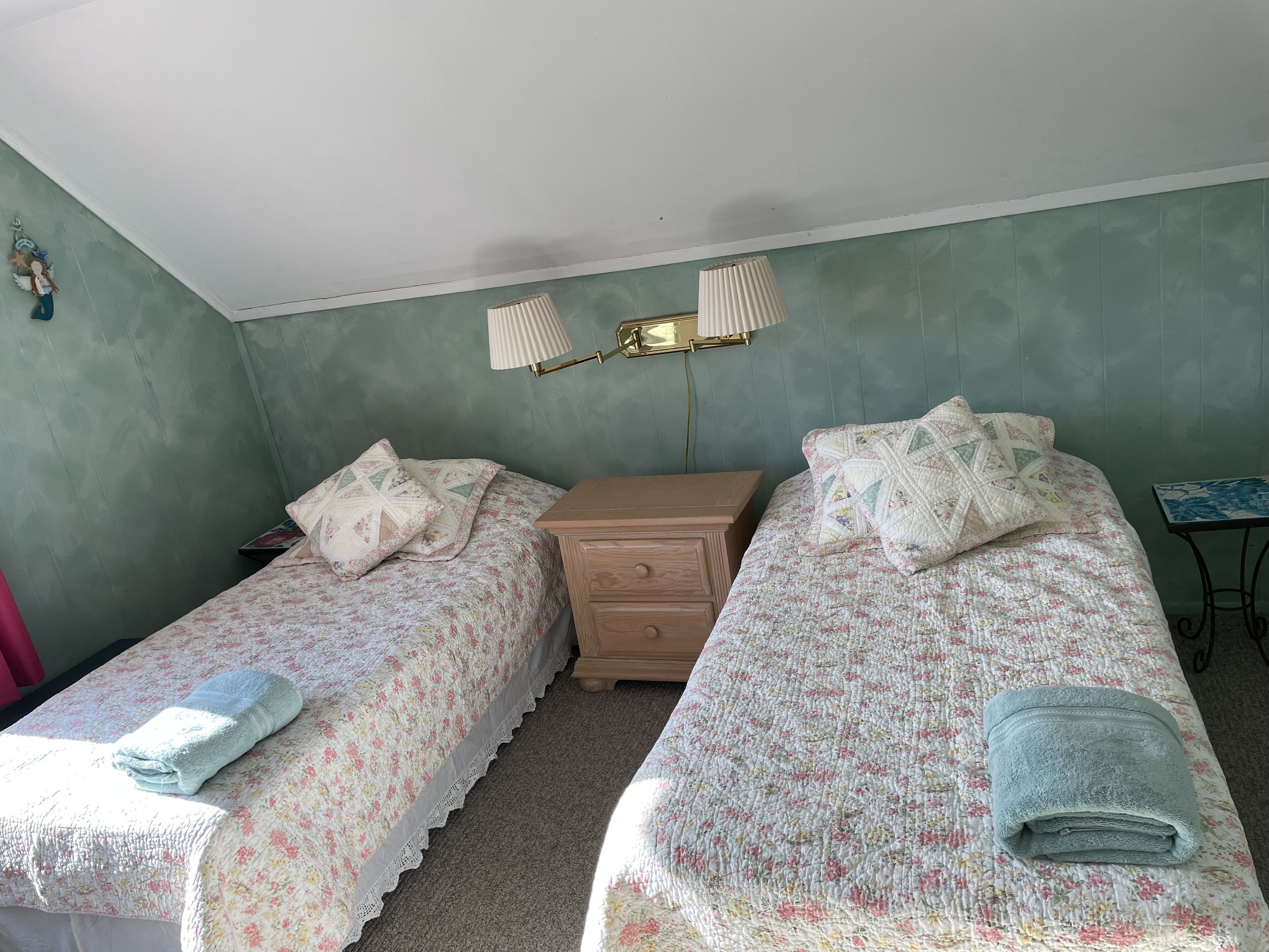 Een slaapkamer met twee eenpersoonsbedden, een nachtkastje, een lamp en een klein tafeltje.